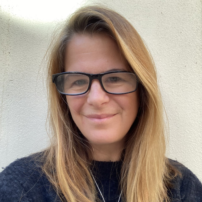 Photograph of Henny, whose bedhead hair clearly didn't get the 'dress code' memo, wearing a big smile, black glasses and a swan necklace