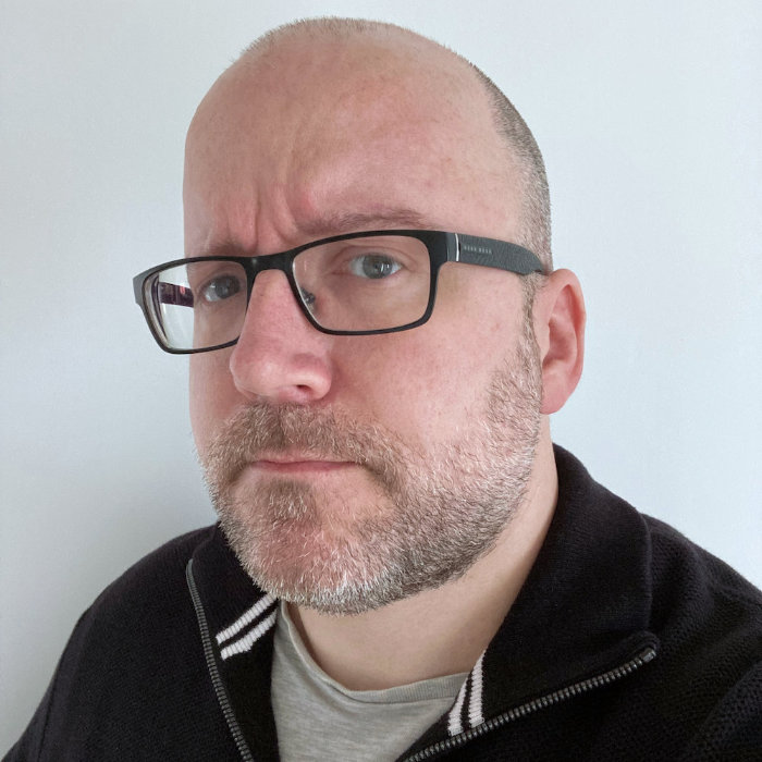 Photograph of Pat, looking thoughtful as he's probably contemplating WACG 2.5.1, with a short, neatly trimmed beard and moustache, wearing glasses with a rectangular black frame and a slight frown