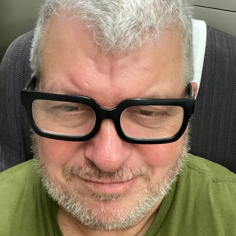 Photograph of Steve, looking mighty and wise, smiling to himself as he looks just off camera with short grey hair and thick black glasses
