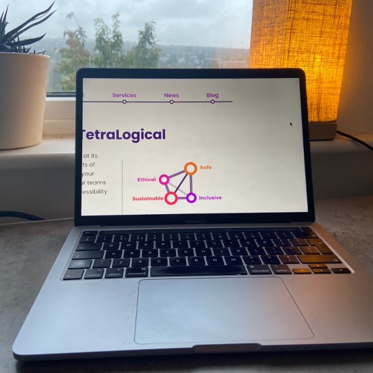 A laptop on a desk showing the TetraLogical homepage zoomed with the main navigation showing in the viewport