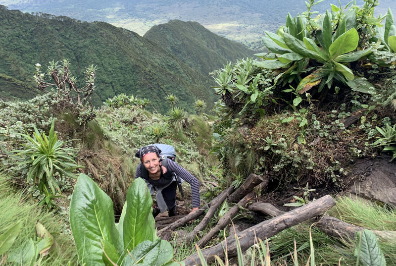 Photograph of Ela smiling while climbing a wooden ladder in a jungle at the side of a mountain