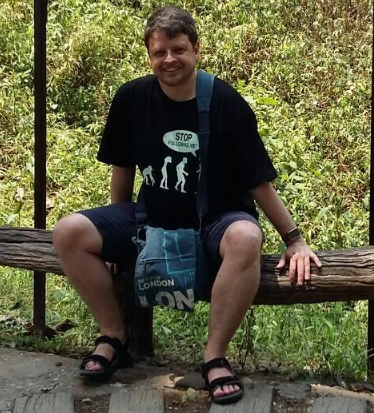 Graeme sat smiling at the camera with the leafy green background of the Thai jungle behind him