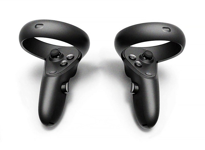 Two handheld controllers made of black plastic with a grip that leads to a circular band. On the side of the grips are a button and a trigger button. On the face of the grips, are a joystick and more buttons