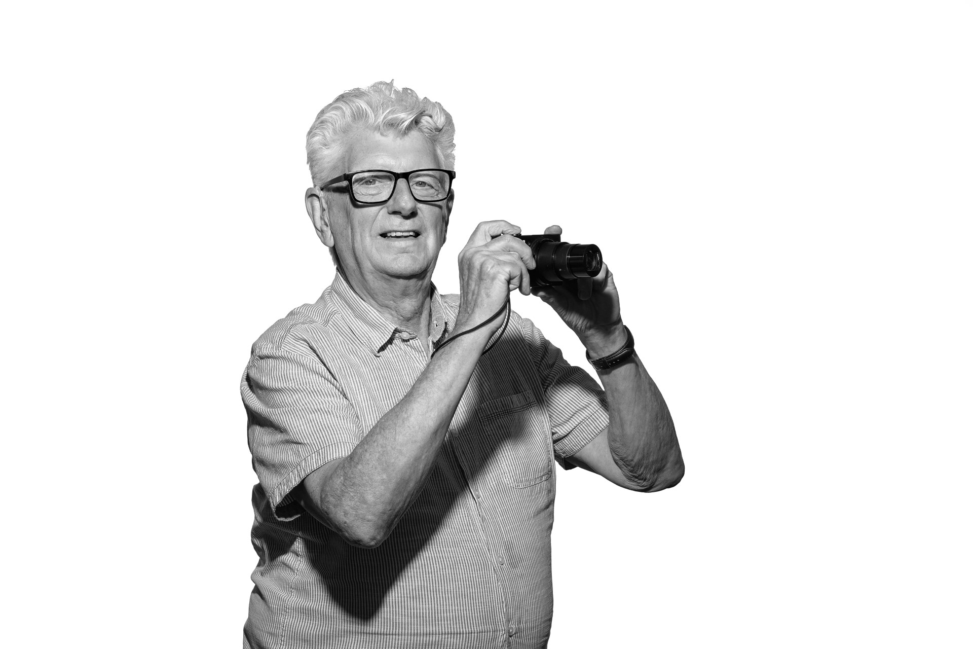 A black and white photo of Steve, an older white man with thick white hair. He is facing into the camera with a slight smile while he holds his own camera up