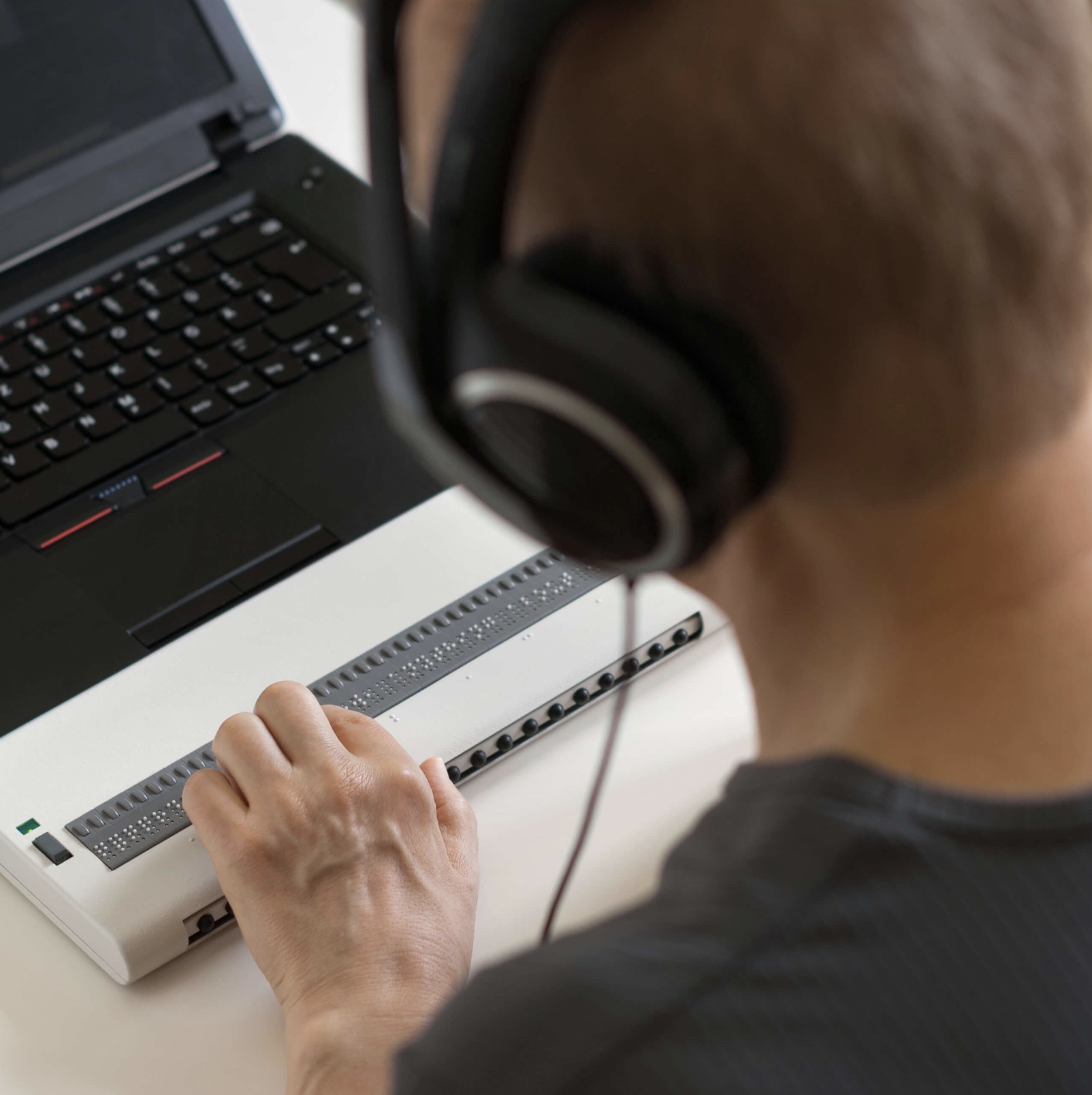 A refreshable Braille display next to a laptop being used by a person wearing headphones