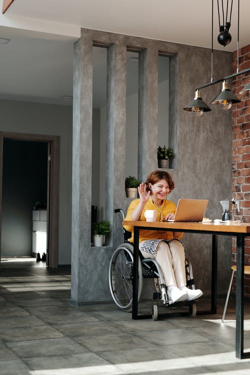 A person in a wheelchair, waiving in front of a laptop